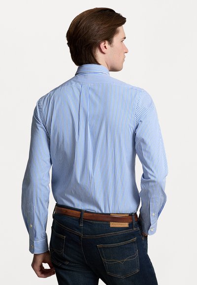 Camicia a righe blu chiaro e bianco, con colletto, polsini con bottone e tessuto liscio. Abbinata a jeans scuri.