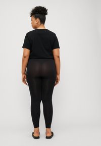 Black cotton t-shirt paired with semi-sheer black leggings. The figure is viewed from the back, focusing on the smooth fabric and fit.