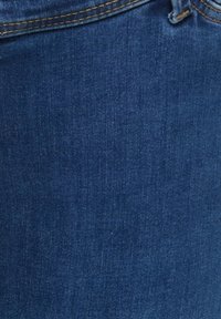 Tissu en denim bleu foncé avec couture visible près du haut, montrant une partie d'une ceinture et une passant de ceinture.