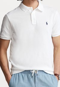 Polo blanc en coton avec un col à revers et une patte de boutonnage à trois boutons. Petit logo bleu marine sur le côté gauche de la poitrine.