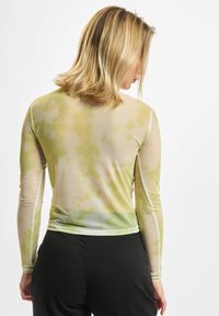 Dlhý rukáv, ľahký top v zeleno-žltej tie-dye vzore, so priliehavým strihom a hladkou, priesvitnou textúrou látky.