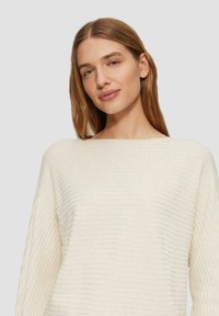 Cremefarbener Pullover mit geripptem Muster, breitem Ausschnitt und lockerer Passform. Der Stoff wirkt weich und leicht.