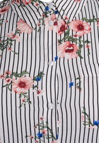 White shirt with black stripes and floral pattern. Features pink and blue flowers, a collar, and white buttons along the front.