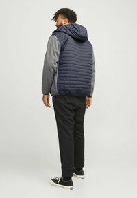 Marineblå quiltet jakke med grå softshellærmer og hætte. Sorte bukser og sneakers fuldender outfittet. Strukturstof og kontrastfarver.