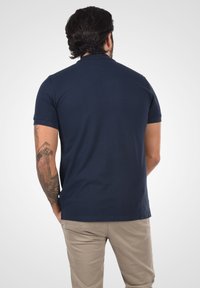 Marineblå piké skjorte laget av bomull med korte ermer, med en klassisk krage og en tettsittende design, parret med lys beige bukser.