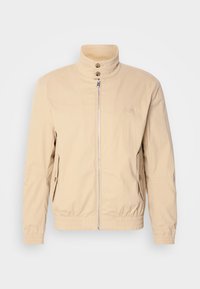 Chaqueta bomber beige con cuello alto, cierre frontal, dos bolsillos laterales, puños elásticos y un logo en el pecho. Tela suave y ligera.