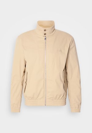 Bežová bomber bunda s vysokým golierom, predným zipsom, dvoma postrannými vreckami, elastickými manžetami a logom na hrudi. Hladká, ľahká tkanina.