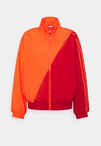 Halv ljusorange och halv mörkröd zip-up jacka med ståkrage, elastiska ärmslut och midja, samt röda ränder på den högra ärmen.