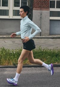 Hele sinine pika varrukaga jooksupaita, mustad lühikesed püksid ja mitmevärvilised jooksujalatsid valgete sokkidega, millel on voolujooneline sportlik disain.
