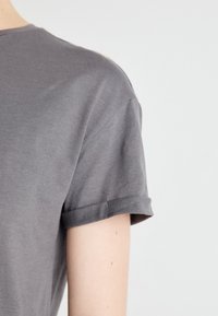 Grå t-skjorte med korte ermer laget av myk bomull, med rullet ermedetalj og et enkelt design uten mønstre eller detaljer.