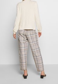 Beige Strickpullover mit langen Ärmeln, kombiniert mit karierten Hosen in Creme, Braun und Grau, die einen lockeren Schnitt und eine Knöchellänge haben.