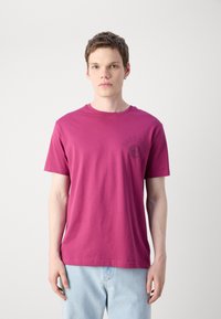 Magenta medvilninis marškinėliai su apvalia iškirpte, trumpomis rankovėmis ir apvaliu logotipo printu ant kairiojo krūtinės. Lygus audinys, standartinio kirpimo.