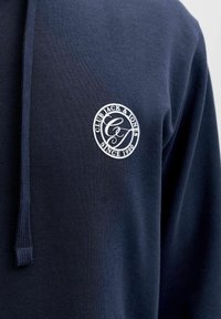 Navy blue cotton hoodie featuring a drawstring, textured fabric, and a round logo with "CLUB JACK & JONES SINCE 1990" in white.