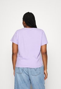 Koszulka z krótkim rękawem w kolorze lawendowym, wykonana z miękkiej mieszanki bawełny, z klasycznym okrągłym dekoltem i prostym wykończeniem u dołu. W zestawie z jasnoniebieskimi dżinsami.