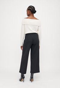 Cremefarbener, schulterfreier Pullover kombiniert mit schwarzen, gestreiften weit geschnittenen Hosen und schwarzen, hohen Stiefeletten. Glatte Strickstruktur, entspannte Silhouette.