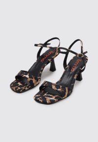 Sandalias de tacón con estampado de leopardo en negro y marrón, con punta cuadrada, tiras finas en el tobillo y tacón cuadrado. Textura suave y diseño minimalista.