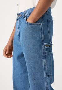 Jeans de mezclilla en azul claro con corte recto. Incluye cierre de botón, bolsillos laterales y una etiqueta de marca en el bolsillo trasero.
