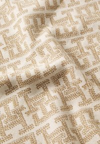 Tessuto intrecciato con uno sfondo crema e un intricato motivo geometrico dorato. Texture morbida con una leggera lucentezza e un design strutturato.