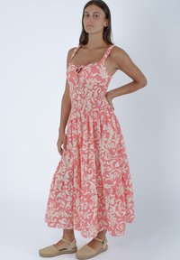 Maxi abito a fiori rosa con corpetto aderente, vita arricciata e gonna a strati. Spalline regolabili e dettaglio a bottoni nella scollatura.