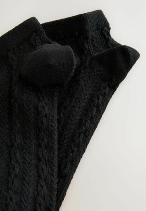 Juodos megztos kojų šiltesnės su tekstūriniais raštais, turinčios storą juostą viršuje ir suapvalintą pūkuotą detalę šone.