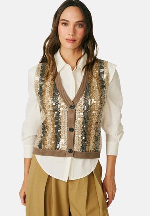Mujer con una camisa blanca abotonada bajo un chaleco de punto con lentejuelas marrón a rayas y pantalones anchos a juego.