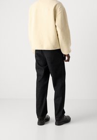 Giacca in fleece crema con superficie testurizzata, abbinata a pantaloni in denim scuri. Scarpe nere completano l'outfit. Vista da dietro.