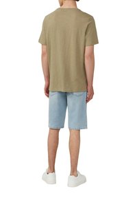 Olivgrünes Kurzarmhemd mit Rundhalsausschnitt, kombiniert mit hellblauen Denim-Shorts, die knapp über dem Knie enden. Weiße Sneaker sind sichtbar.