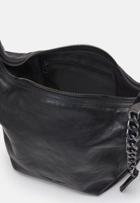 Sort lædertaske med en blød tekstur, åbnet for at afsløre et glat interiør og en lynlåslomme; har en kædeaccent på remmen.