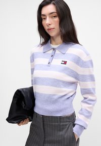 Pulover tricotat cu dungi orizontale de culoare violet deschis și crem, cu guler și trei butoane. Pata cu logo pe piept.