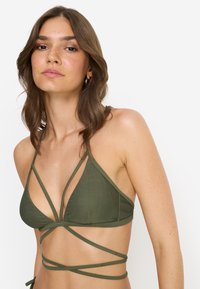 Τριγωνικό τοπ μαγιό σε ελιά πράσινο με λουριά που διασταυρώνονται. Ομαλή υφή, μίνιμαλ σχεδιασμός, τονίζοντας την προσαρμοζόμενη εφαρμογή και την κάλυψη.