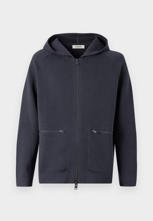 Tamsiai tamsiai mėlynokos spalvos gobtuvu užsegama striukė. Pagaminta iš minkštos medžiagos, su dviem priekinių kišenių užtrauktukais ir raglaninėmis rankovėmis, suteikiančiomis lankstumo.