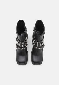 Bottines noires à bouts carrés, en cuir, avec des sangles cloutées argentées et des fermetures éclair sur le côté. Texture lisse et semelle épaisse.