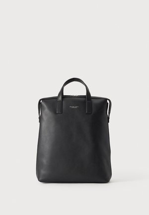 Sac cabas noir en cuir Michael Kors avec deux courtes anses et une fermeture zippée sur le dessus, sur un fond clair.