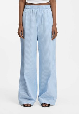 Jasnoniebieskie spodnie o szerokich nogawkach z cienkimi białymi pionowymi paskami, elastycznym paskiem w talii, noszone z czarnymi sandałami na obcasie z odkrytymi palcami i białym krótkim topem.