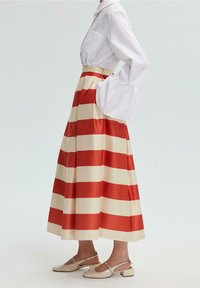 Blouse blanche à manches évasées associée à une longue jupe rayée rouge et crème. La jupe est longue, fluide, avec une taille ajustée.