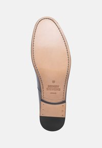 La semelle de chaussure en cuir présente une surface lisse beige avec un talon en caoutchouc noir. Bordure cousue avec le logo embossé "HENRY STEVENS".