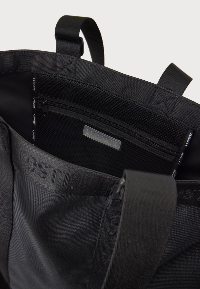 Borsa tote Lacoste nera con manici strutturati, tasca interna con cerniera in rete e nome del marchio in rilievo sulla tracolla in tessuto.