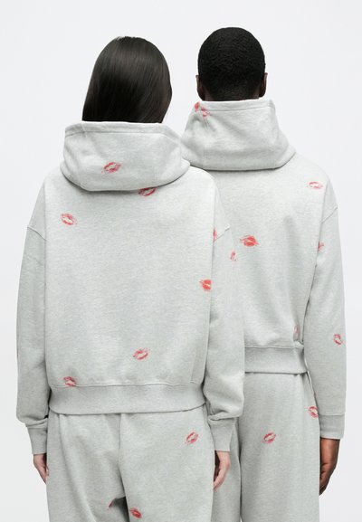 Grå huvtröja med luva, med röda läppstiftsavtrycksmönster. Mjuk textur, avslappnad passform och ribbade muddar och nederkant.