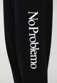 Black sweatpants featuring white vertical text that reads "No Problemo" along the left leg. Soft fabric with a relaxed fit.