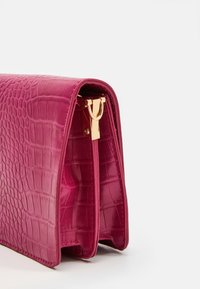 Fuchsia handbag with a crocodile texture, featuring a gold hardware clasp and a structured design. Opened view shows interior lining.