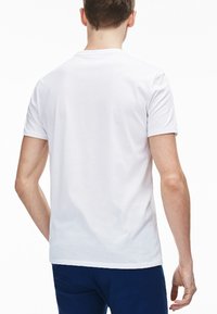 Hvid bomulds t-shirt med korte ærmer og rund hals, set fra ryggen. Glat tekstur og enkelt design uden synlige logoer.