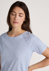 Light blue t-shirt with white polka dots, soft fabric, round neckline, and short sleeves. Smooth texture with a relaxed fit.