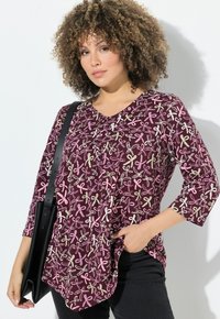 Top burdeos con escote en v y mangas de tres cuartos, con patrones de lazo multicolores. Llevado con pantalones negros y un bolso negro.