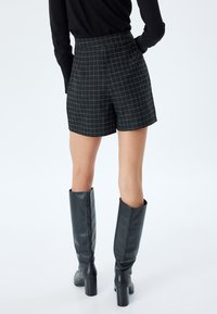 Pantaloni neri con un motivo a griglia bianca, design a vita alta, tessuto morbido, abbinati a stivali in pelle neri fino al ginocchio.