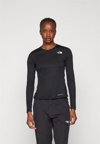 Maglietta nera a maniche lunghe realizzata in tessuto testurizzato, con un piccolo logo bianco sul petto e un'etichetta all'orlo.