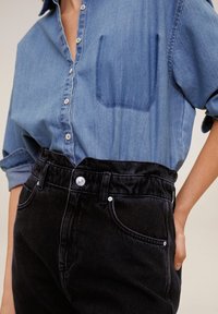 Chemise en denim bleu clair avec une poche poitrine, design à boutons; associée à un jean noir taille haute avec des coutures prononcées et une fermeture à bouton.