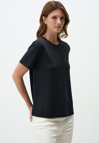 T-shirt nera a maniche corte realizzata in tessuto morbido, con collo rotondo e vestibilità morbida, abbinata a pantaloni di colore chiaro.