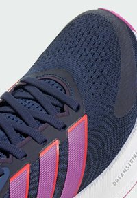 Buty sportowe z siateczkową górą w ciemnoniebieskim kolorze, różowymi i czerwonymi akcentami, teksturowanymi nakładkami i wzorzystą podeszwą. Sznurowadła w dopasowanym kolorze.