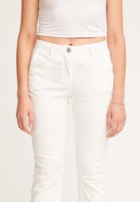 Pantaloni in misto cotone bianchi con silhouette aderente, presentano una chiusura con bottone e tasche laterali, texture liscia, abbinati a un top corto.