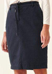 Jupe bleu marine jusqu'aux genoux avec taille à cordon, devant plat et poches latérales, fabriquée dans un tissu léger et texturé.